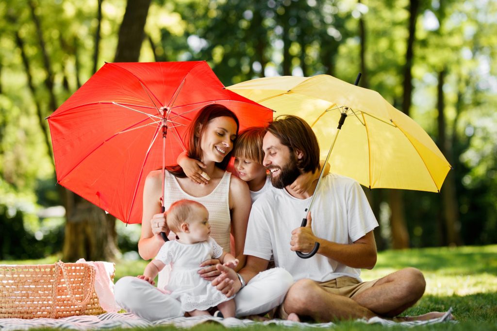 Sitting under bright red and yellow umbrellas family dressed in the in the white clothes have a rest