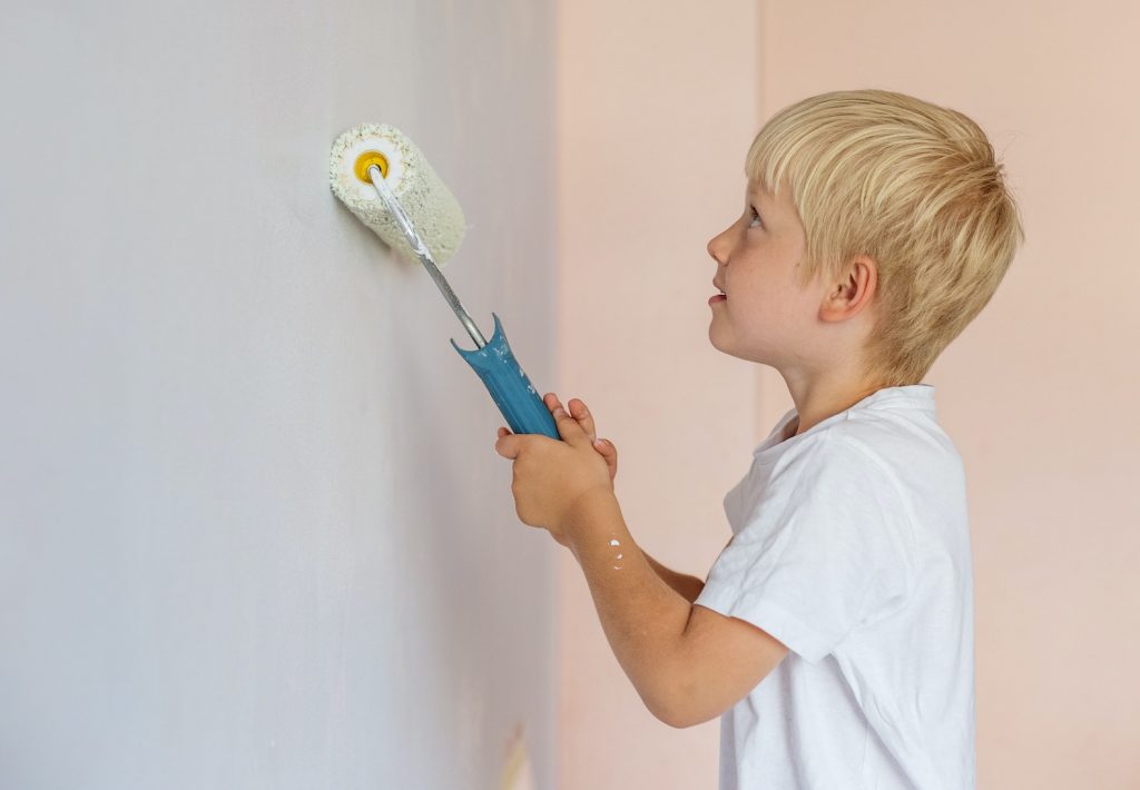 Happy kid helps parents to paint wall. New house for family. Home renovation.